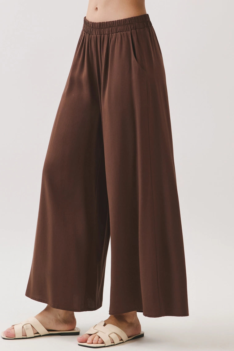 Brown wide leg pants with elastic waistband, styled with cream slide sandals, front view.