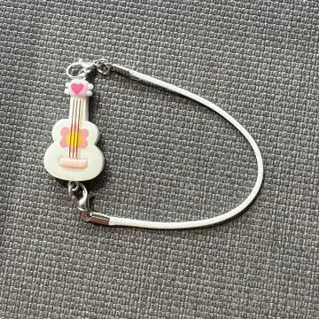 A small, white guitar-shaped doll accessory with pink and yellow accents, attached to a metal loop.