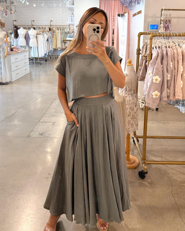 Woman taking a mirror selfie wearing a gray outfit in a clothing store.