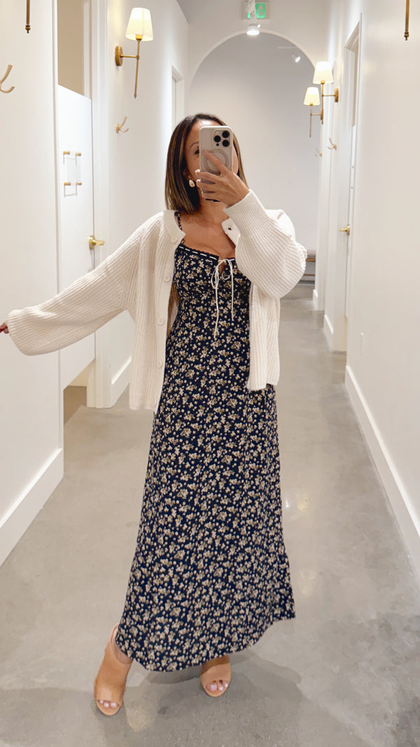 Woman in a floral dress and white cardigan standing in a hallway.