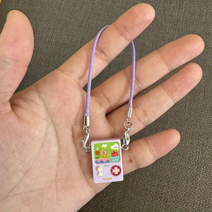 A small, colorful game-themed charm on a purple cord, with cartoon-style graphics and a silver clasp, for attaching to Labubu dolls or other accessories.