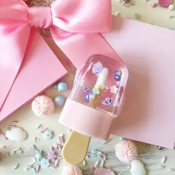 A pink popsicle-shaped lip gloss with colorful sprinkles and a ribbon bow on the packaging.
