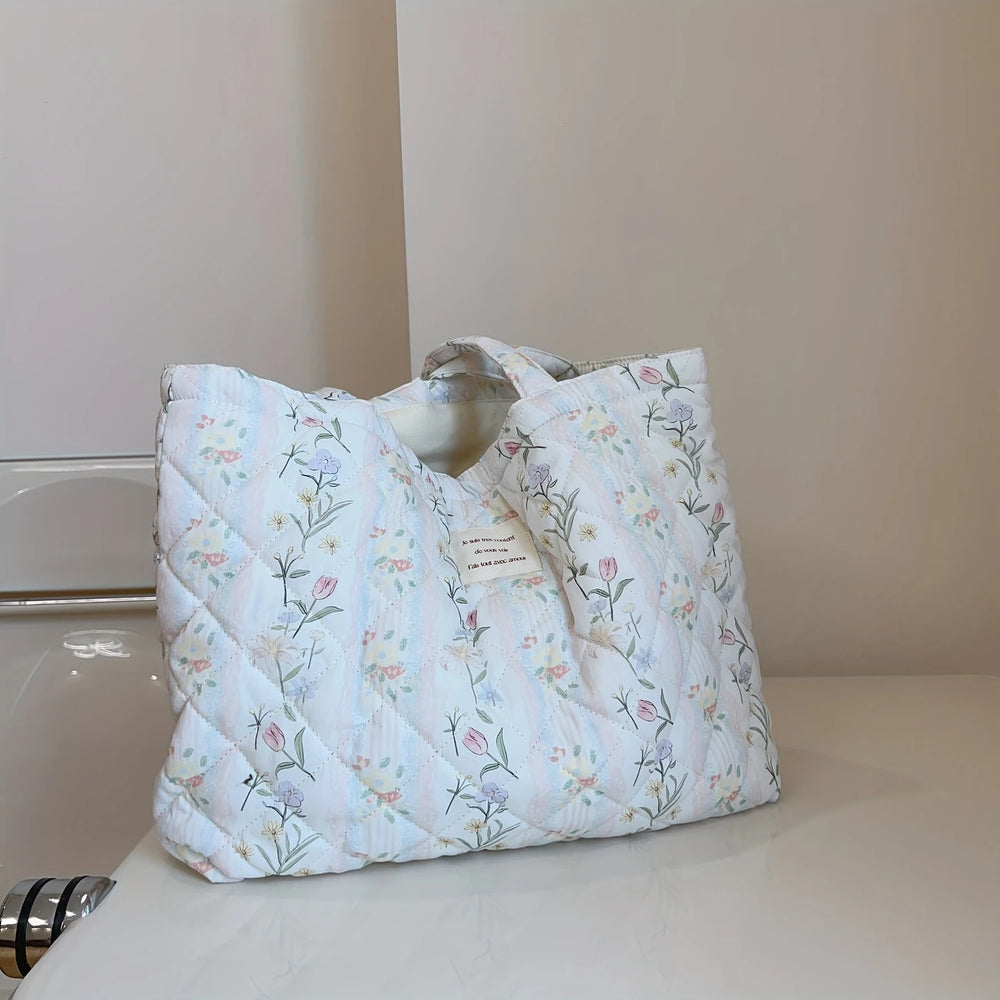 A white quilted tote bag with a floral print, featuring an interior pocket and a zipper closure.