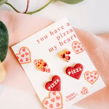 Vibrant red and pink pizza-themed stud earrings with heart and pizza slice designs, featuring a whimsical "You have a pizza my heart" message.