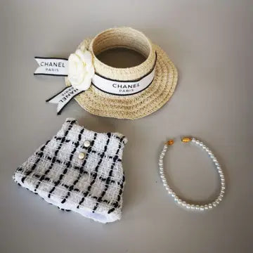 Elegant straw hat with Chanel branding, textured tweed shorts, and a pearl necklace - a refined, vintage-inspired luxury fashion ensemble.