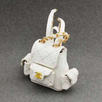 A white, quilted backpack with golden hardware and flower details, designed as a stylish accessory for a doll.